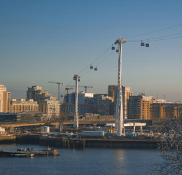 Cable car gondolas travel above a waterfront skyline with construction cranes and residential buildings.