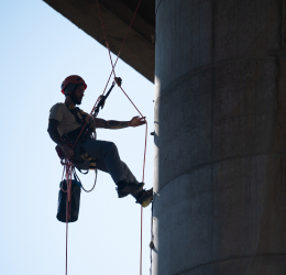 A worker in safety harness and helmet rappels down a large concrete pillar.