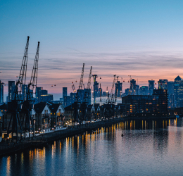 Dockside cranes silhouetted against a city skyline at dusk, with lights reflecting on the water.
