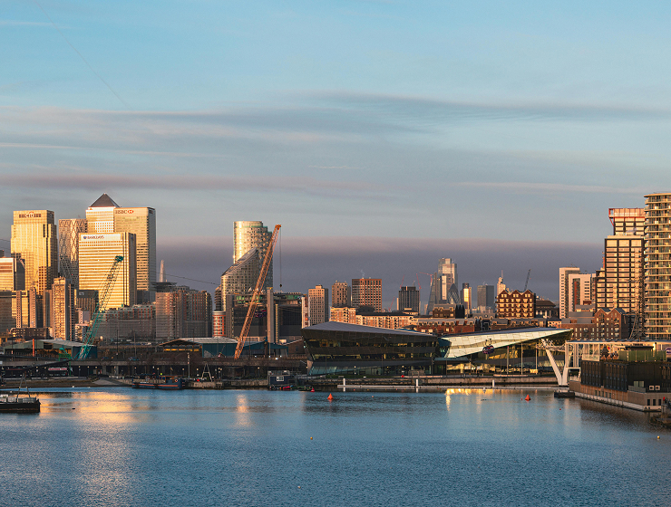 City skyline with high-rise buildings and a cable-stayed bridge, viewed across the water at golden hour.
