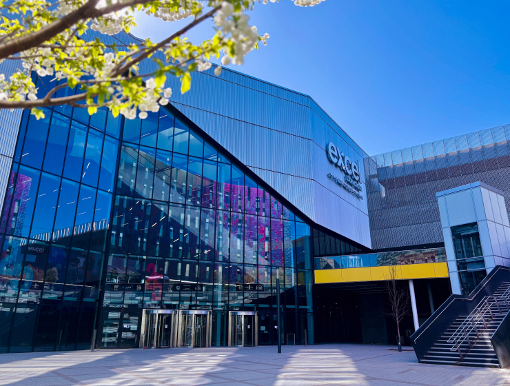 Exterior of the ExCeL London exhibition centre, with blossom branches framing the glass façade.