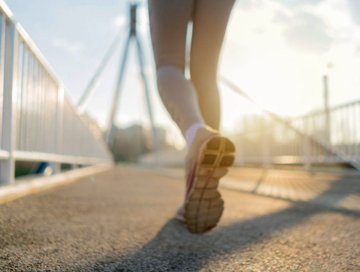 A person running across Connaught Footbridge at sunset.