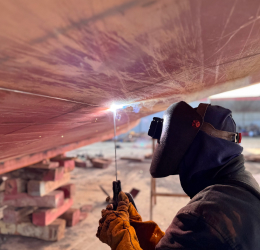A welder in a protective mask works on dock edge repairs.