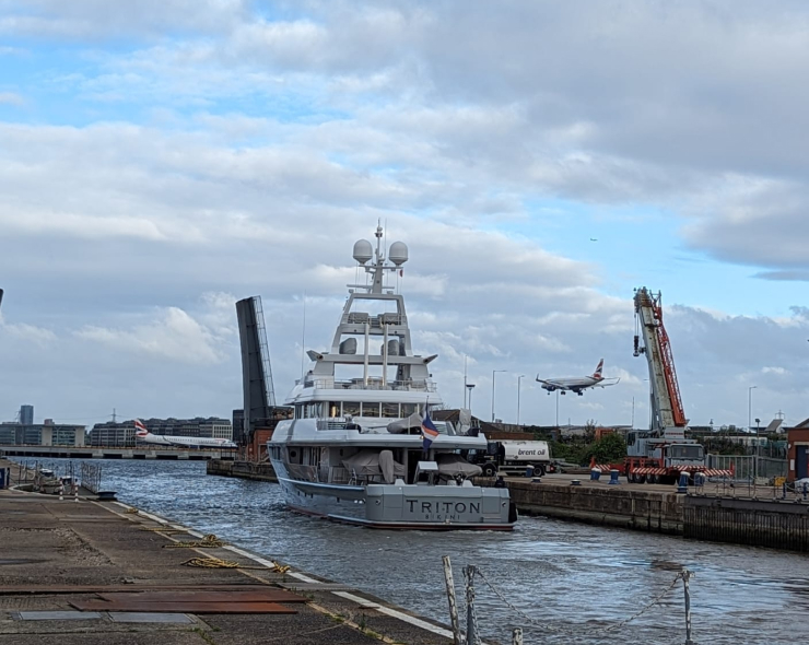 A yacht docked at the waterfront, with a plane landing in the background.