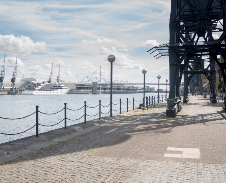 A dockside promenade with cranes and a docked ship along the waterfront.