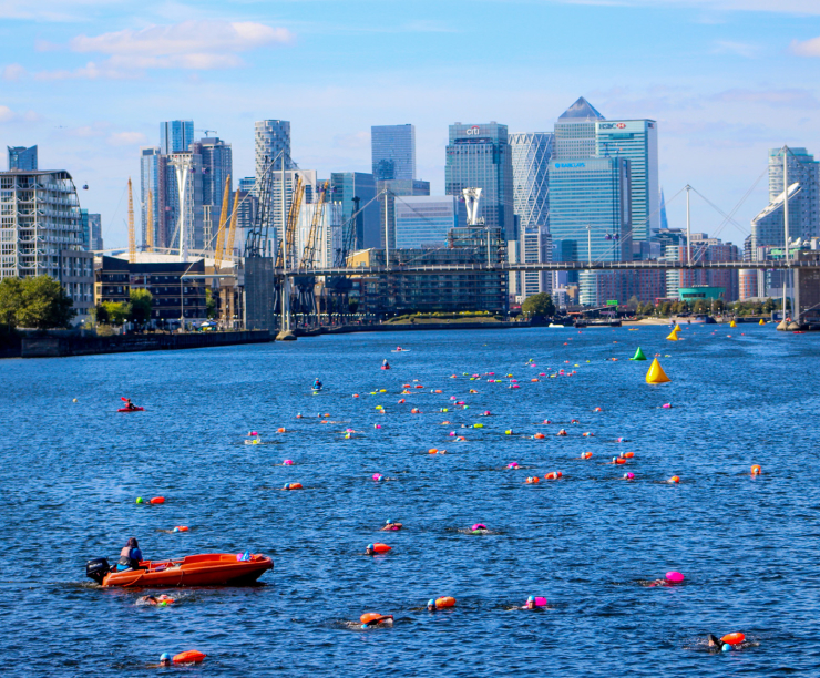 Open water swimmers with a safety boat, Canary Wharf skyline behind.