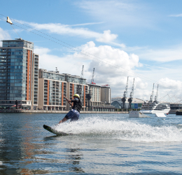 A cable wakeboarder on the dock, buildings and cranes behind.